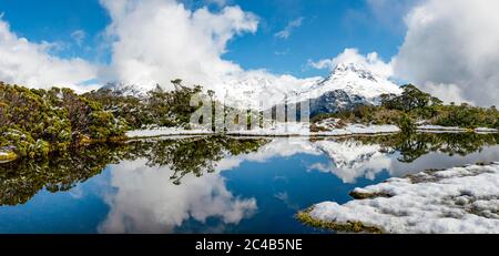 Piccolo lago di montagna con riflessione, vista sulle montagne ricoperte di nuvole, neve alla cima della Key Summit, Mt. Christina, Parco Nazionale di Fiordland, Ovest Foto Stock