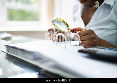 Revisore che indaga sulle frodi aziendali utilizzando la lente d'ingrandimento in ufficio Foto Stock