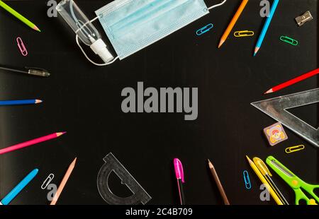 Vari materiali scolastici, maschera facciale e gel idroalcolico su lavagna. Concetto di ritorno a scuola dopo la pandemia di covid19. Foto Stock