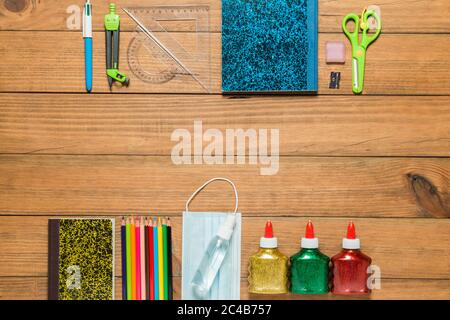 Vari materiali scolastici, maschera facciale e gel idroalcolico su tavole di legno. Concetto di ritorno a scuola dopo la pandemia di covid19. Foto Stock