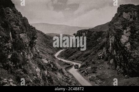 Una scena dei primi anni '20 con una vettura classica nel Passo di Keimaneigh, una burrone precipitosa tra le cime di Foilstookeen e Doughill nei Monti Caha tra Macroom e Bantry. Originariamente fotografato da Clifton Adams (1890-1934) per 'Ireland: The Rock Whence i was hewn', una rivista nazionale di geografia dal marzo 1927. Foto Stock