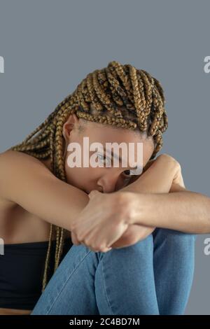 Triste giovane afroamericano che le tiene le ginocchia, appoggiando la testa sulle braccia Foto Stock