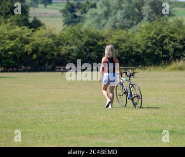 Una donna che cammina con la sua bicicletta attraverso l'erba al Teston Bridge Country Park. Il 25 giugno 2020 è stato il giorno più caldo dell'anno. Foto Stock