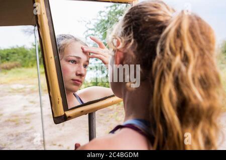 Ragazza di tredici anni che guarda nello specchio di un campo teso, applicando la protezione solare alla sua fronte Foto Stock