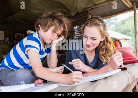 Fratello e sorella che fanno i compiti insieme in un campo teso in Botswana Foto Stock