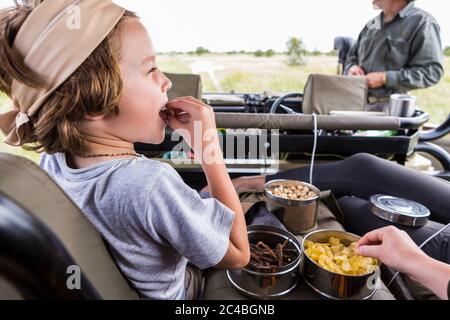 Ragazzo di 6 anni che mangia spuntini in un veicolo safari, Botswana Foto Stock