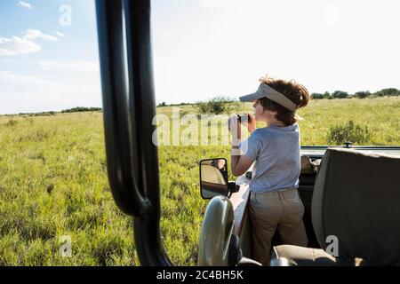 Un ragazzo di sei anni con binocolo in un veicolo da safari Foto Stock