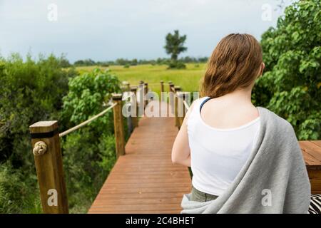 vista posteriore di una ragazza di 13 anni che cammina su un sentiero in legno in un campo di safari Foto Stock