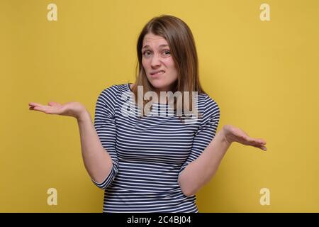 Attraente giovane donna che si struggisce le spalle sul muro giallo. Foto Stock