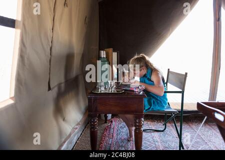 Una ragazza di dodici anni seduta su una scrivania in una tenda in un campo di riserva naturale, disegnando. Foto Stock