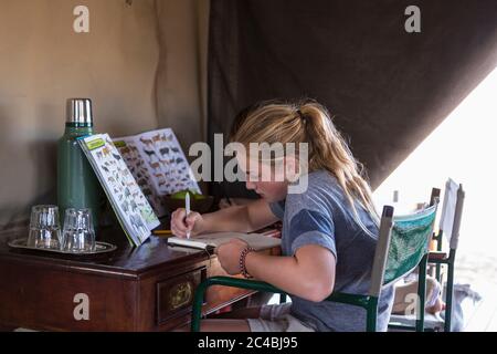 Ragazza di dodici anni seduta in una tenda, scrivendo o disegnando in un giornale. Foto Stock