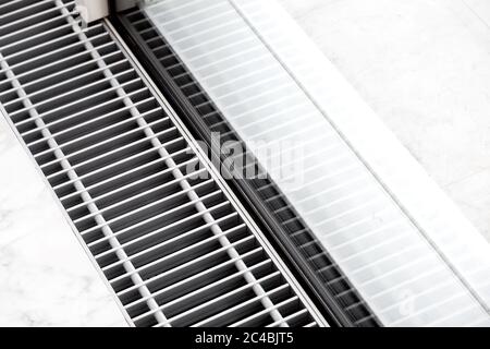 Griglia di riscaldamento con ventilazione a pavimento in pietra bianca vicino alla finestra panoramica, primo piano della griglia dell'aria condizionata. Foto Stock