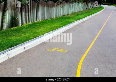 strada asfaltata con corsia per biciclette con simbolo di bicicletta e marcatura gialla con marciapiede sul lato del prato con sistema di drenaggio e legno Foto Stock