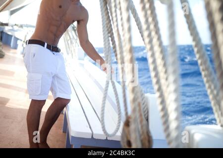 Uomo senza senso che indossa pantaloncini bianchi sul ponte di una barca a  vela, rigging Foto stock - Alamy