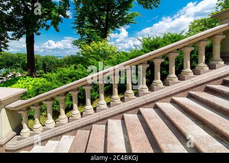 ringhiera in pietra con balaustre alla scala in granito nel cortile con piante verdi in una giornata di sole con un cielo blu, nessuno. Foto Stock