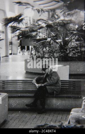 Bella fotografia in bianco e nero degli anni '70 di un vecchio che legge un libro al centro commerciale locale. Foto Stock