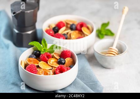 Minuscoli pancake con cereali, mirtilli, lamponi, menta e miele per colazione Foto Stock