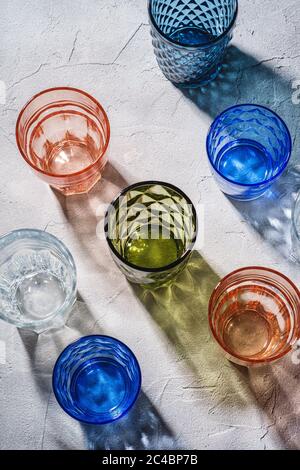 Colorato sfaccettato e geometrico bicchiere da bere, gruppo di verde vuoto, rosso, blu e trasparente beverage su fondo di pietra calcestruzzo, angolo Foto Stock