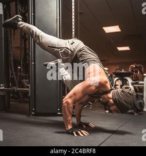 Un uomo sportivo con il portatore in palestra sta facendo esercizi di yoga. Posizione sui bracci. Benefici mentali dello yoga. Ardha Bakasana o posa di corvo.. Una posizione di bilanciamento gamba Foto Stock