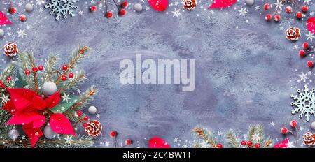 Sfondo panoramico natalizio, piatto con ramoscelli, poinsettia, bacche e trinket. Decorazioni natalizie rosse e verdi su sfondo scuro a trama. Foto Stock