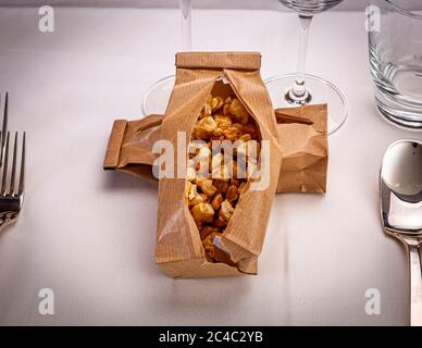 Un dessert gourmet di pezzi dorati e croccanti si trova in due sacchetti incrociati di carta marrone aperti su un tavolo apparecchiato con una tovaglia bianca durante la cena di gala "Level Null" (livello zero) all'Hotel e Ristorante Kronenschlösschen di Hattenheim, Eltville am Rhein, Assia, Germania. Una forchetta si trova a sinistra, un cucchiaio a destra. Dietro ci sono dei bicchieri. La cena di gala "Level Null" (livello zero) della sera del 1° marzo 2017 fa parte del 21° Festival Gourmet & Vino del Rheingau. I pasticceri Andy Vorbusch (Hotel The Dolder Grand, Zurigo) e René Frank (CODA Dessert Bar, Berlino) servono un menu di cinque portate Foto Stock