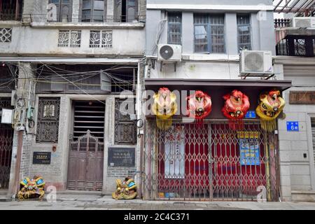 Un edificio storico di Guangzhou con la sua tradizionale porta a pali scorrevoli in legno vecchio stile e testa di leone´s di fronte alla casa. Foto Stock