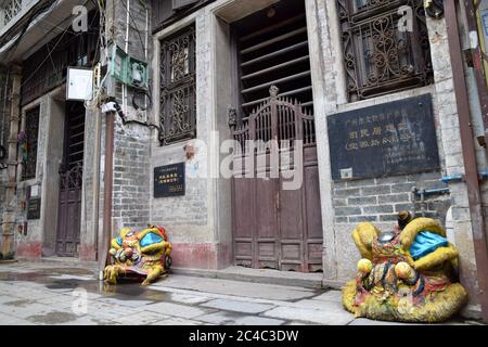 Un edificio storico di Guangzhou con la sua tradizionale porta a pali scorrevoli in legno vecchio stile e testa di leone´s di fronte alla casa. Foto Stock