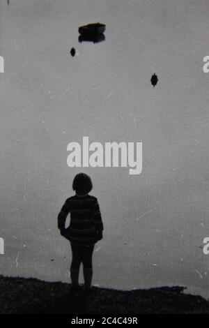 Fine anni '70 vintage contatto stampa in bianco e nero fotografia di un bambino in piedi alla fine di un molo che guarda le acque ferme. Foto Stock