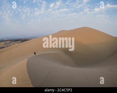 giovane uomo che sale una duna nel deserto, nuvole e cielo blu Foto Stock
