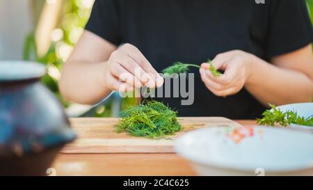 Primo piano delle mani delle donne scopa green da bastoni e li mette sul tagliere. Foto Stock