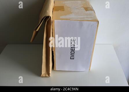 Fuoco selettivo sul segno DI PROVA attaccato alla scatola di cartone in posizione verticale posto su tavola di legno vicino alla busta marrone con luce solare e ombra Foto Stock