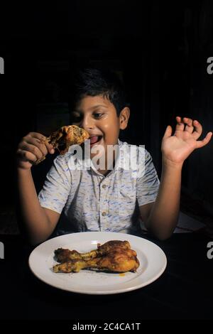 Indiano Kid mangiare pollo fritto drumstick. Bambino che ha un briciola di pollo da mangiare. Bambino con arrosto di pollo yummy. Foto Stock