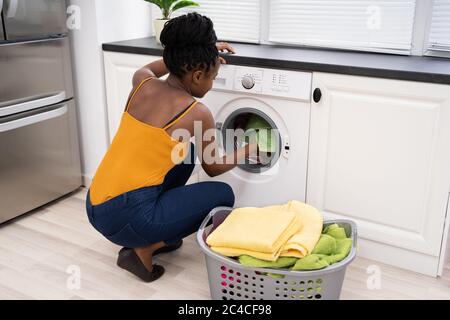Donna di carico panni sporchi in lavatrice per il lavaggio in una camera di servizio Foto Stock