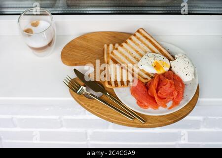 Menu colazione: Pane tostato, salmone affumicato, uova in camicia e tazza di caffè sul davanzale bianco Foto Stock