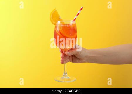 Mano femminile con bicchiere di aperol Spritz cocktail su sfondo giallo Foto Stock