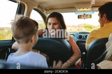 Buona guida con la famiglia in auto. Donna che gioca con i suoi bambini seduti sul sedile posteriore della macchina. Foto Stock