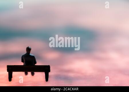 Figurine in miniatura posata come uomo seduto da solo su una panchina in scenario surreale, immagine minimalista concetto astratto Foto Stock