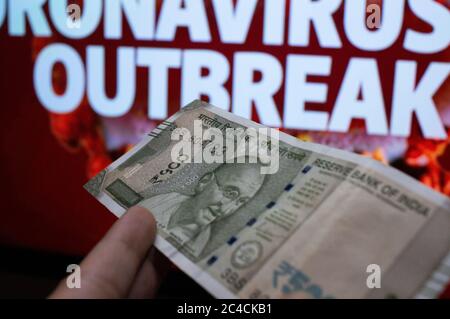 Gurgaon India Circa 2020 : Fotografia di una nota di valuta della Rupee 100 indiana tenuta da una mano davanti ad una tavola con coronavirus scritto nel colo rosso Foto Stock