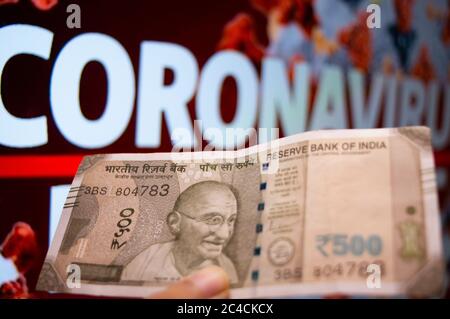 Gurgaon India Circa 2020 : Fotografia di una nota di valuta della Rupee 100 indiana tenuta da una mano davanti ad una tavola con coronavirus scritto nel colo rosso Foto Stock