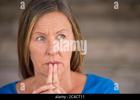 Portrtait attraente donna religiosa matura pregando con le mani piegate, premuroso, speranzoso, meditante, sfondo sfocato, spazio di copia. Foto Stock