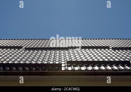 Pendenza del tetto coperta da lastre metalliche effetto piastrelle di colore marrone scuro. Foto Stock