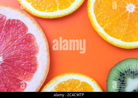 Fondo agli agrumi, fette di pompelmo, kiwi, mandarino. Modello estivo con spazio per la copia, spazio vuoto per il testo, sfondo arancione brillante Foto Stock