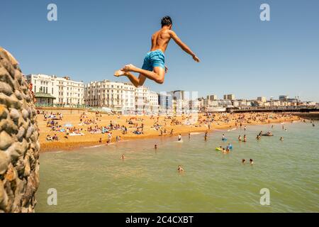 Un giovane che salta in mare in una giornata calda a Brighton Foto Stock