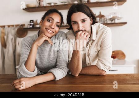 Uomo attraente e bella donna afroamericana sorridente appoggiata sul tavolo che guarda felicemente in macchina fotografica insieme. Giovane coppia internazionale sognata Foto Stock