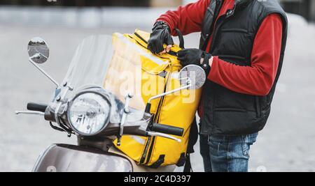 Corriere irriconoscibile con sacchetto di consegna sullo scooter che consegna il cibo all'esterno Foto Stock