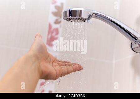 le mani controllano la temperatura dell'acqua della doccia. una mano dell'uomo sotto un flusso di fuoco selettivo dell'acqua Foto Stock