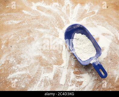 farina di grano bianco sparsa su un tavolo di legno marrone e paletta di plastica blu, vista dall'alto Foto Stock