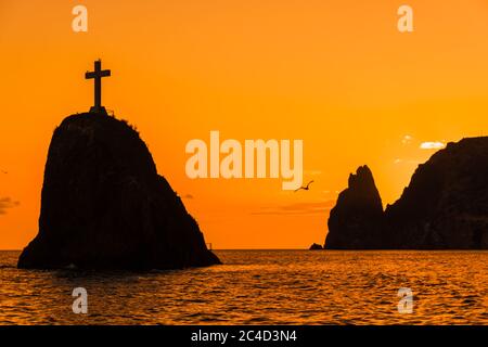 Un tramonto rosso ardente con la silhouette di una scogliera sul mare Foto Stock