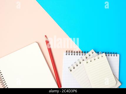 matita di legno rosso e pila di quaderni a spirale con fogli bianchi bianchi bianchi bianchi su sfondo blu, vista dall'alto Foto Stock