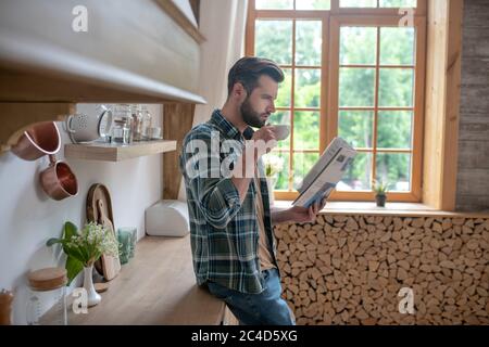 Uomo alto in una camicia a scacchi che ha il caffè e che legge un giornale Foto Stock